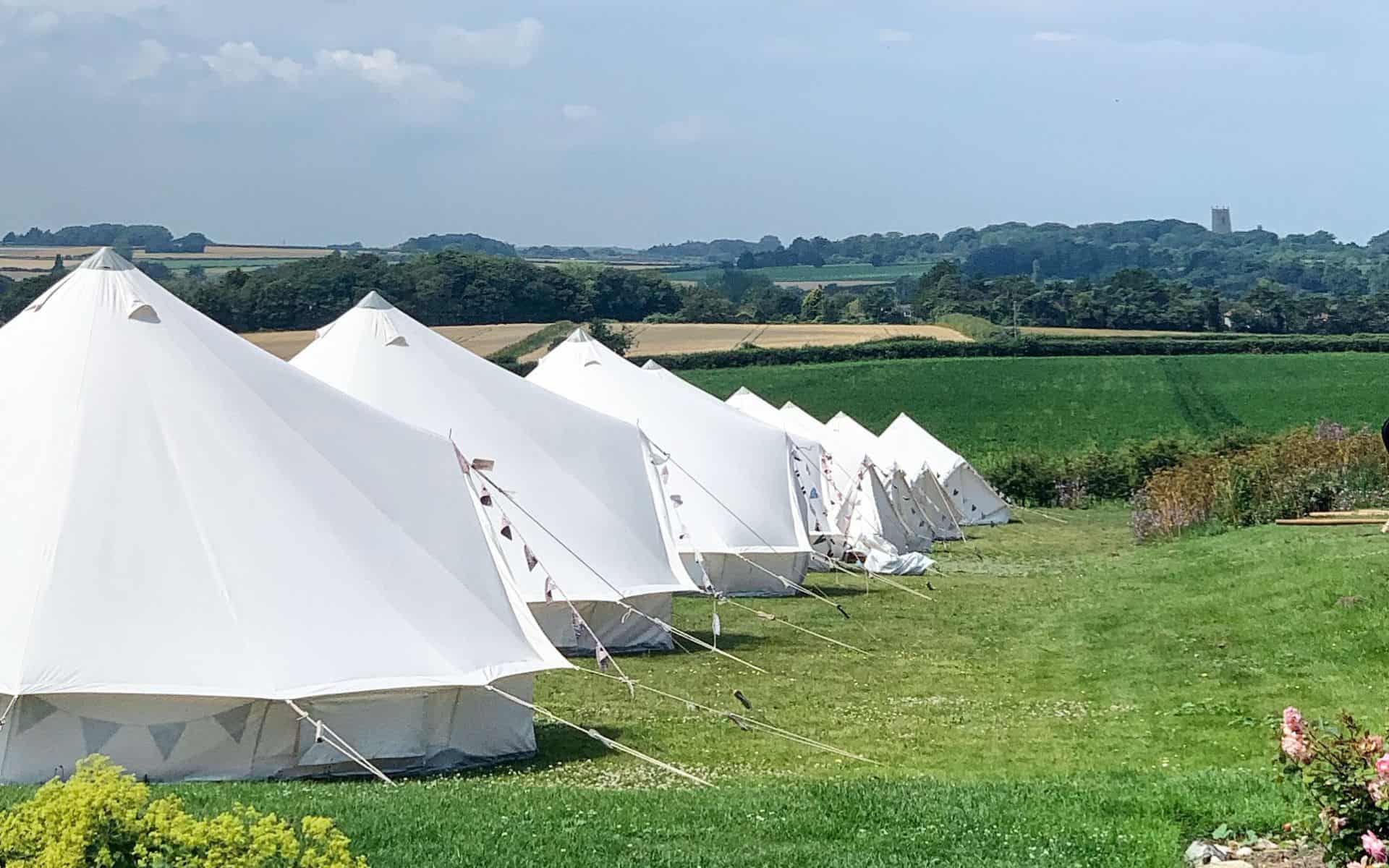 Traditional white bell tents set up on lush green grass in Norfolk for camping.