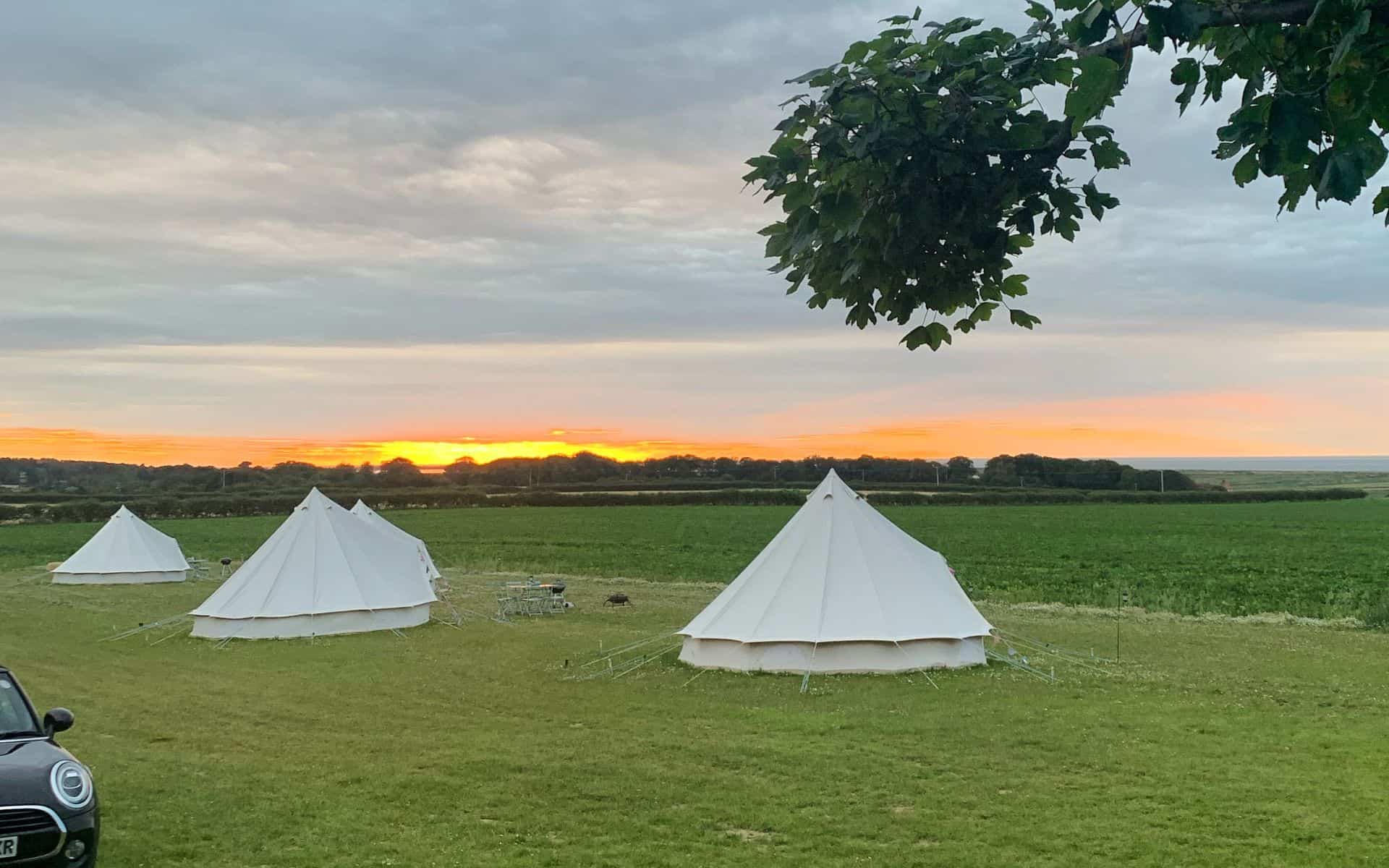 Relaxing camping scene at Barn Drift Norfolk with white tents at sunset.