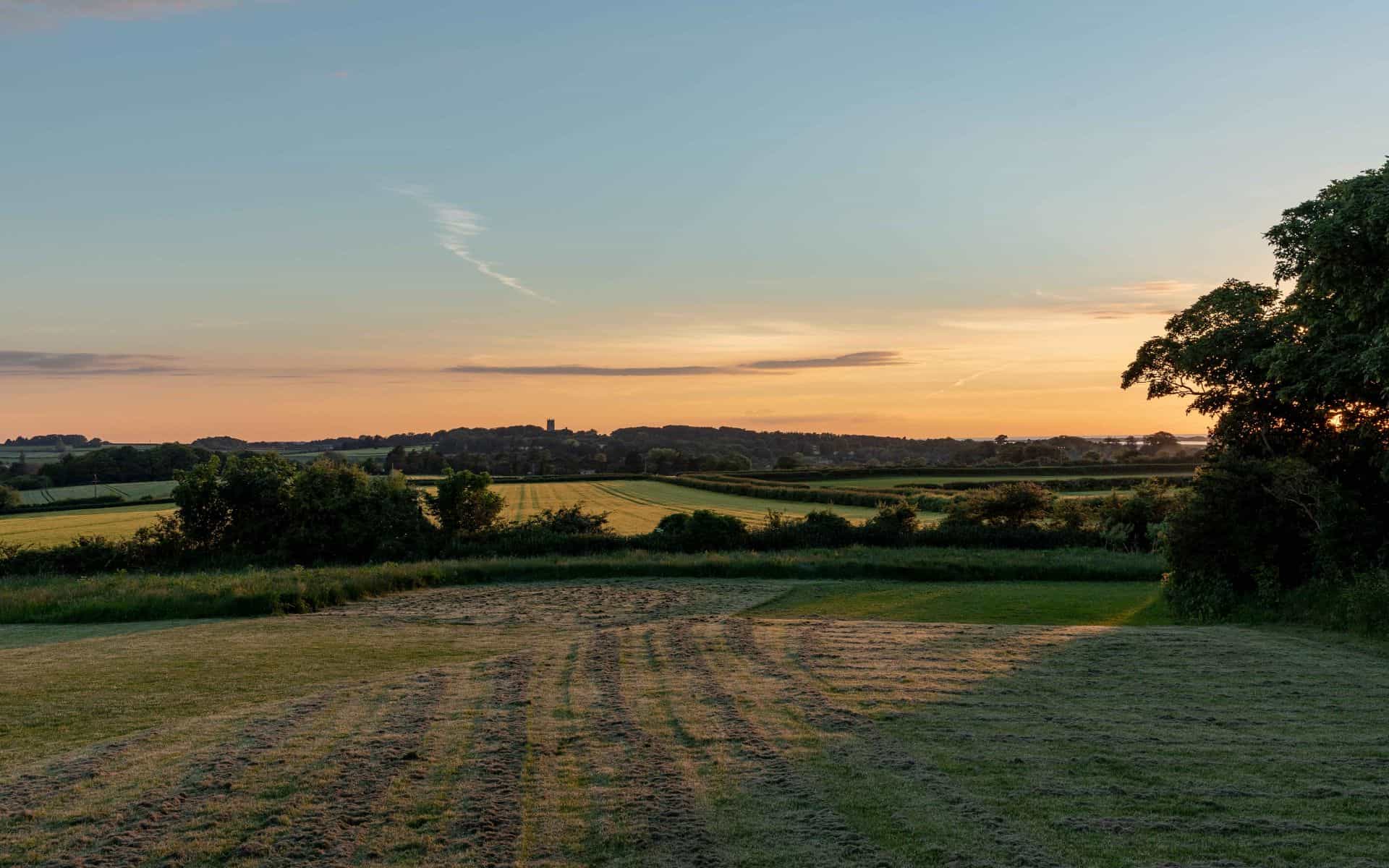 A lush Norfolk countryside landscape at sunset, ideal for camping and outdoor activities.