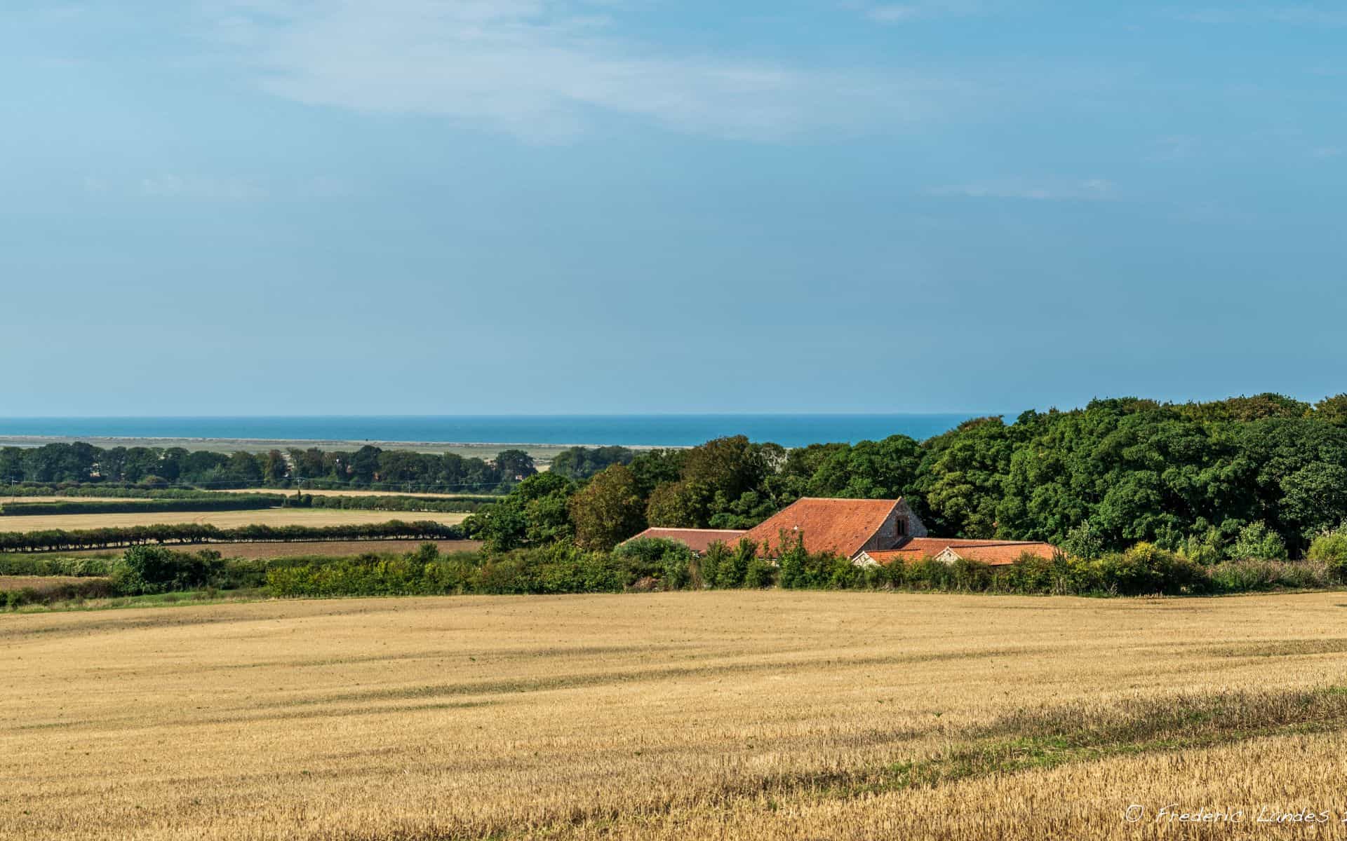 Scenic Norfolk countryside ideal for camping, featuring open fields, lush greenery, and distant sea views.