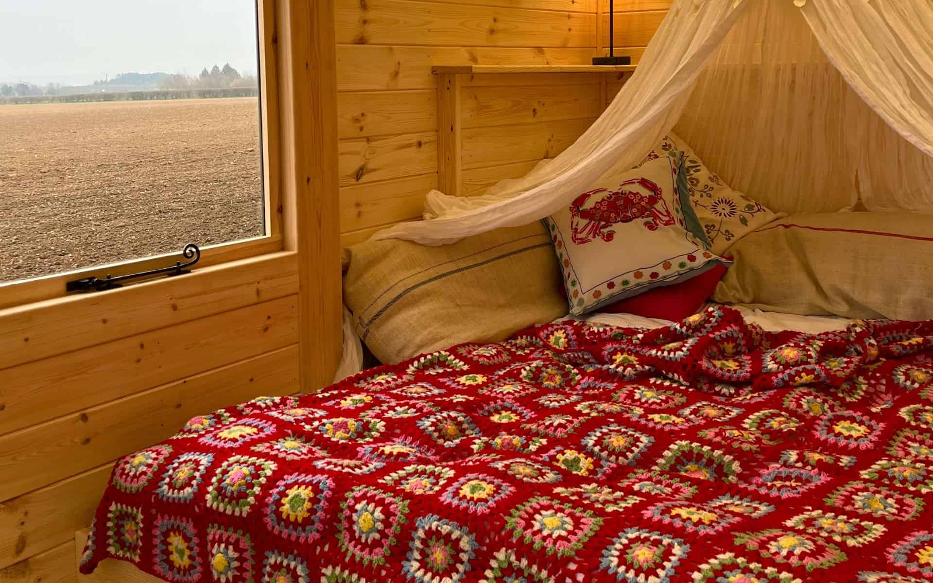 A cozy wooden bedroom with a bed featuring a colourful crochet blanket and decorative pillows, overl.