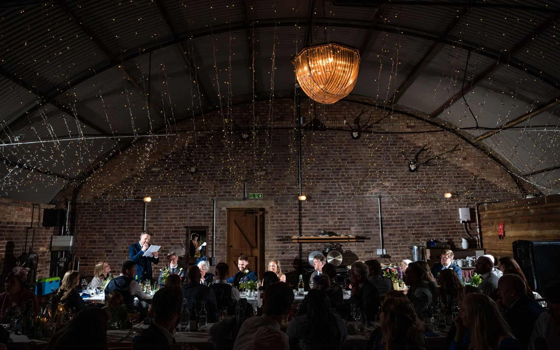 Elegant event space inside The Hanger at Barn Drift Norfolk with string lights and chandelier.