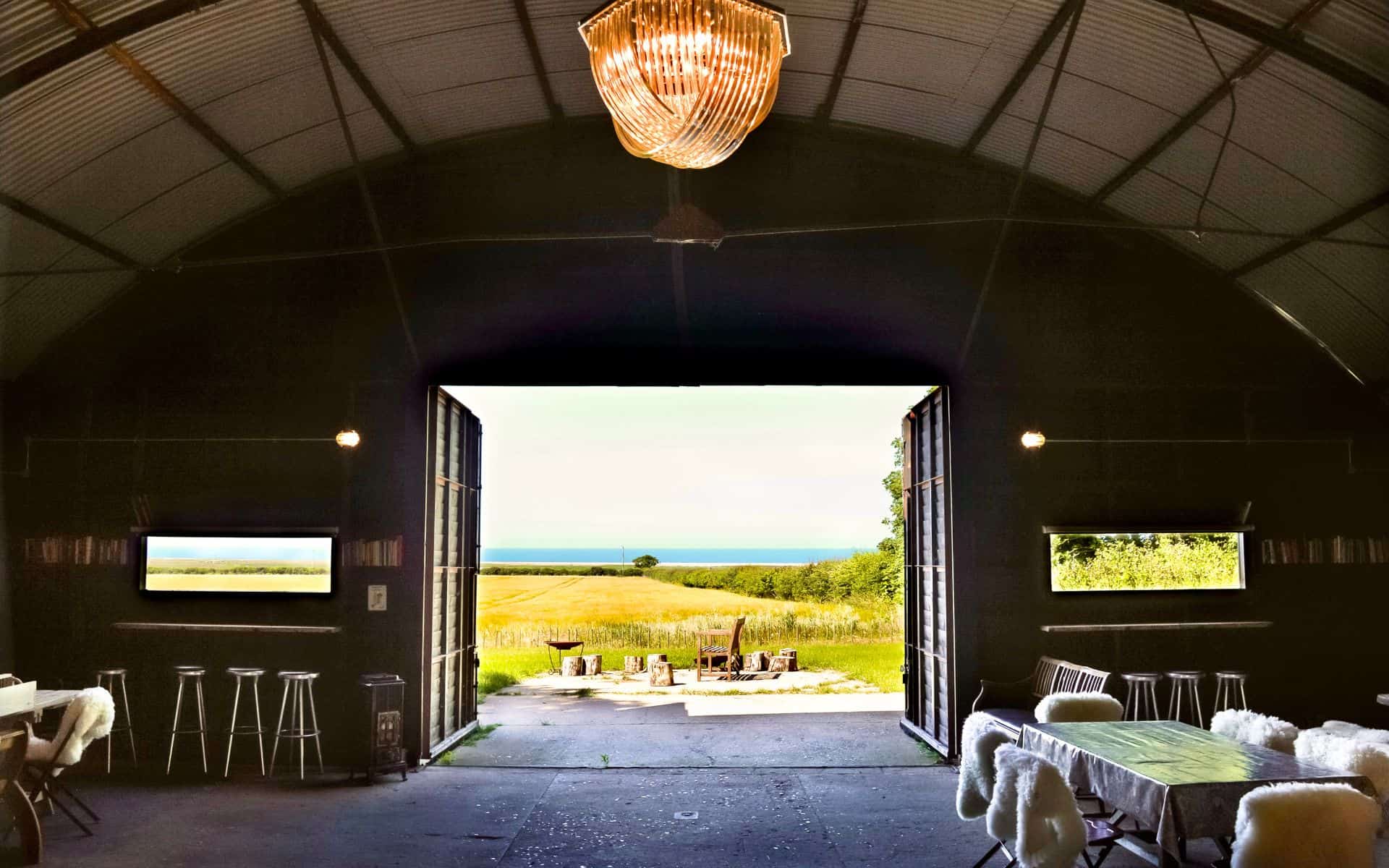 A lush countryside view from inside The Hanger at Barn Drift Norfolk, with open barn doors revealing.