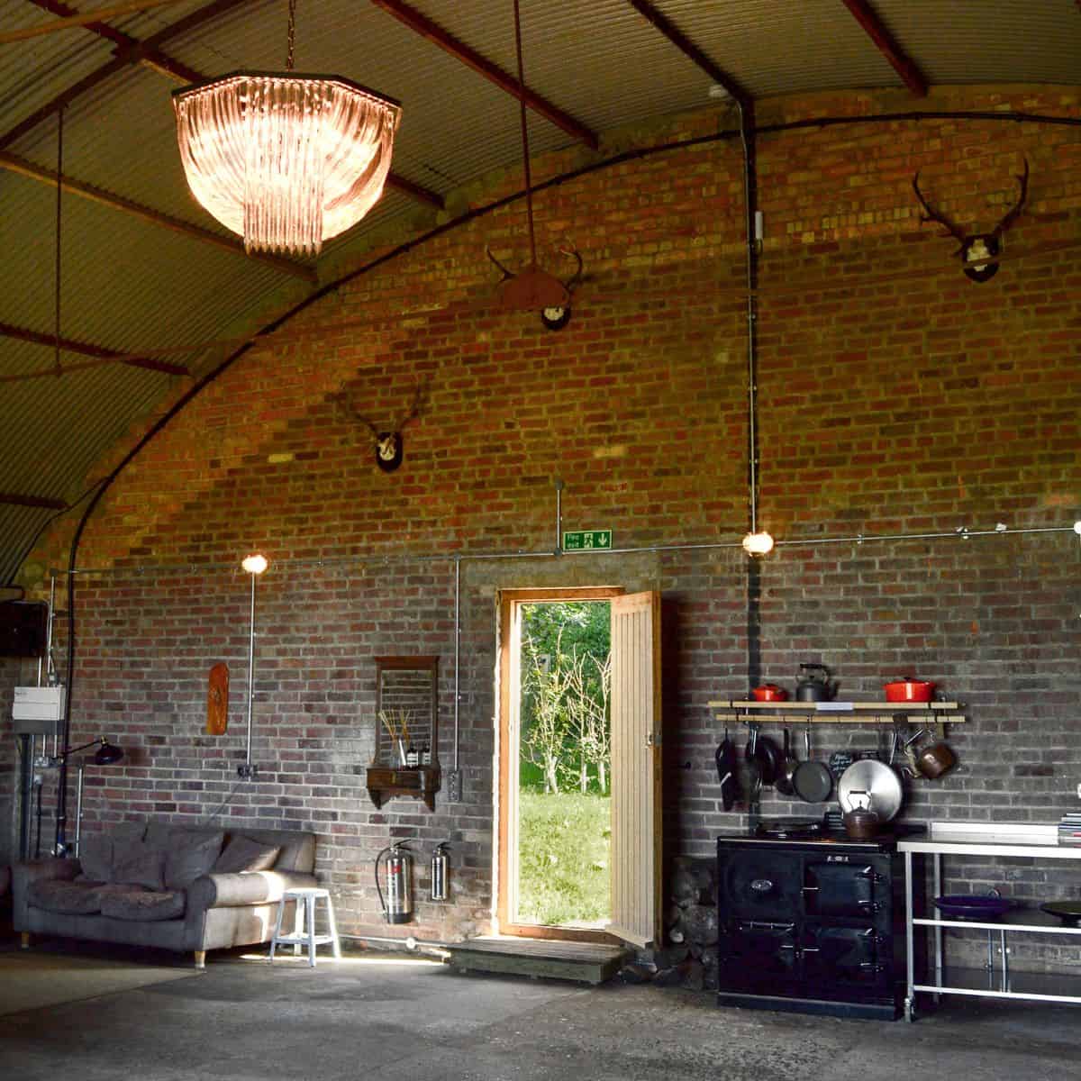 Rustic barn interior with exposed brick walls and vintage kitchen appliances, illuminated by a chand.