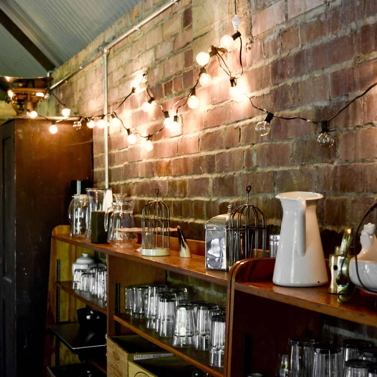 Vintage glassware and decorative lighting on a wooden shelf at The Hanger, Barn Drift, Norfolk.