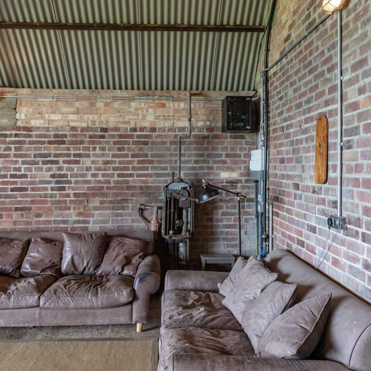 Relaxed seating area inside The Hanger at Barn Drift Norfolk with vintage-style brick walls and comf.