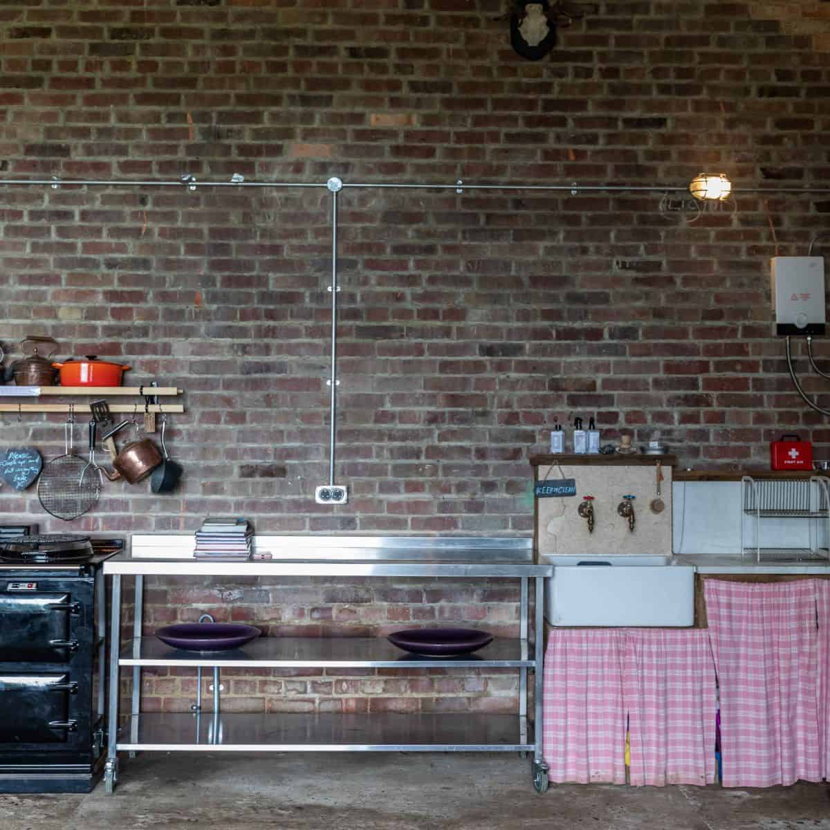 Rustic kitchen with brick wall, vintage sink, and open shelving in Norfolk barn conversion.
